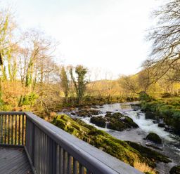 A balcony with a wooden railing overlooking a river with rocks and trees at Pen y Bont Near Mallwyd