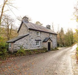 A stone cottage by a road surrounded by trees at Pen y Bont Near Mallwyd