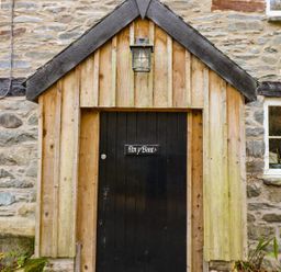 A black door with a wooden porch and a lantern on a stone house at Pen y Bont Near Mallwyd