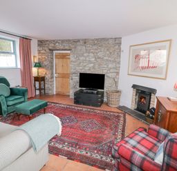 A living room with a stone wall a wooden door a television a fireplace and patterned rugs at The Old Rectory Coach House in Rathmullan County Donegal