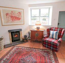 A sitting room with a red plaid armchair a wooden cabinet with a lamp a fireplace and a patterned rug at The Old Rectory Coach House in Rathmullan County Donegal