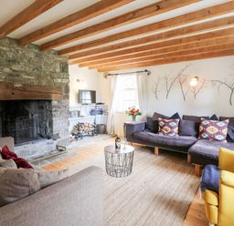 A living room with wooden beams on the ceiling a stone fireplace sofas a yellow armchair a round coffee table and a window at Heron House Talley near Llandeilo