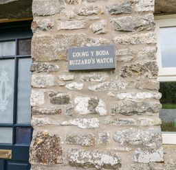 A stone wall with a sign reading Buzzards Watch next to a door and window at Buzzards Watch Talley near Llandeilo