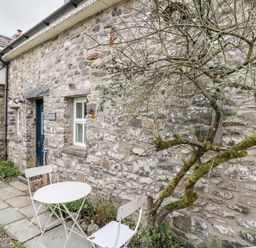 A stone cottage exterior with a small round table and two chairs outside and a leafless tree at Buzzards Watch in Talley near Llandeilo