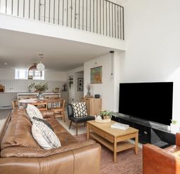 A living room with brown leather sofas a wooden coffee table and a large television with an open kitchen and dining area at Ysgol Fach Little School in Benllech