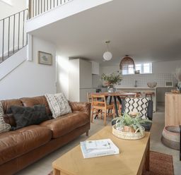 An open living room and kitchen with a brown leather sofa pillows wooden dining table and chairs plants and a wooden coffee table at Ysgol Fach Little School Benllech