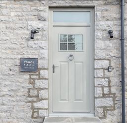A grey door with window panes and a knocker on a stone wall with a sign reading Ysgol Fach little school at Ysgol Fach Little School in Benllech