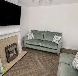A living room with two green sofas a fireplace and a wall mounted television at 39 Mariners Quay Port Talbot