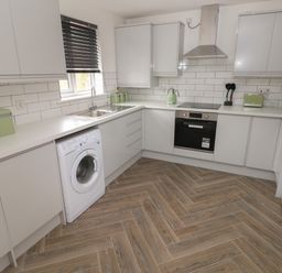 A kitchen with white cabinets a washing machine an oven a sink window and wooden floor at 39 Mariners Quay in Port Talbot