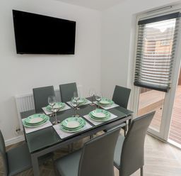 A dining room with six chairs around a glass table set with plates and wine glasses and a wall mounted TV at 39 Mariners Quay in Port Talbot