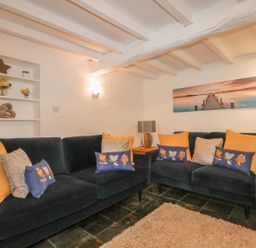 A living room with two dark sofas with various cushions a side table with a lamp and wall art at Blacksmiths Cottage in Crantock