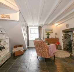 A sitting room with a striped armchair a stone fireplace and shelves by a window at Blacksmiths Cottage in Crantock