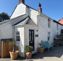 Exterior view of a white stone cottage with a black door blue bench and potted plants at Blacksmiths Cottage in Crantock