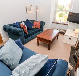 A living room with blue sofas, a wooden coffee table, a wall-mounted TV, and a fireplace at Pentira in Kuggar
