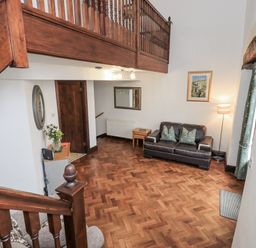 A living room with a sofa and staircase at Horse and Farrier Barn Newton in Cartmel near Cartmel