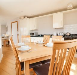 A kitchen and dining area with a wooden table set with dishes and glassware at 23 Tibbys Way in Southwold