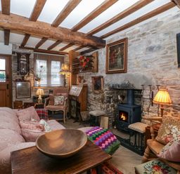 A living room with exposed wooden beams stone walls wood burning stove and various chairs at Hoarders Cottage in Hay-On-Wye