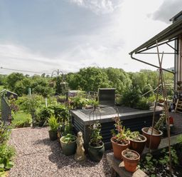 An outdoor garden area with potted plants a wooden bench gravel paths and trees in the background at Hoarders Cottage in Hay-On-Wye