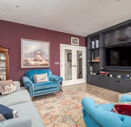 A living room with blue and gray sofas a patterned rug a painting on a purple wall and a built-in black shelving unit with a television at The Stables in Wheatley
