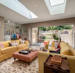 A living room with yellow sofas and a pink ottoman opening to an outdoor stone patio at The Stables in Wheatley