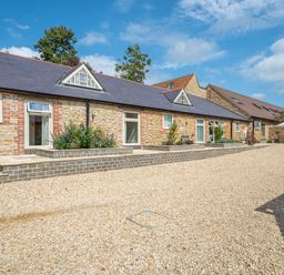 A stone building with multiple windows and a gravel courtyard at The Stables in Wheatley