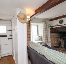 A living room with a sofa a stone fireplace wooden beams and plaid curtains at Dormouse Cottage in Burton Bradstock