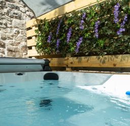 A hot tub in an outdoor area with a stone wall and plants at Wonderland in Tweedmouth, Berwick-Upon-Tweed
