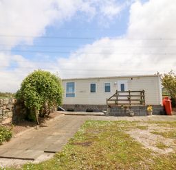 A mobile home with a small wooden deck and potted plants in a garden with paved walkway and stone wall at Gwel Y Mor in Nasareth near Caernarfon