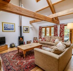 A living room with wooden beams a wood burning stove sofas a wooden coffee table and glass doors opening to a garden at Bridge Cottage in Dalwood