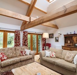 A living room with two patterned sofas wooden beams and large windows at Bridge Cottage in Dalwood