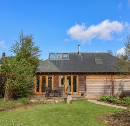 A backyard with green lawn and patio furniture in front of a wooden house at Bridge Cottage in Dalwood