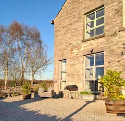 A stone building with large windows chairs potted plants and a barbecue outside at The Dairy at Brackenthwaite Farm Arnside