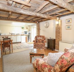 A living room with floral armchairs a wooden coffee table a dining table and a kitchenette with appliances at Pear Tree Barn in Stalham