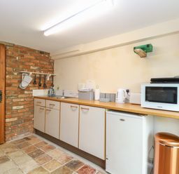 A kitchen with a wooden door brick wall cabinets microwave fridge and trash bin at Pear Tree Barn in Stalham