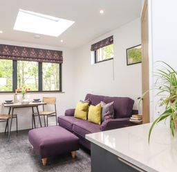 A small dining table with two chairs near windows and a purple sofa with cushions in a living area at Yew Tree Cabin in Ullswater