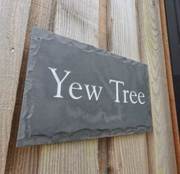 A wooden wall with a dark stone sign that says Yew Tree at Yew Tree Cabin Ullswater