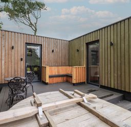 An outdoor deck area with wooden walls a wooden bench metal table and chairs at Yew Tree Cabin in Ullswater