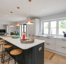 A kitchen with an island and bar stools with windows above the sink at Greystones in Upton St Leonards