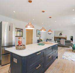 A kitchen with an island counter with copper pendant lights and a stainless steel refrigerator at Greystones in Upton St Leonards