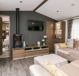 A living room with a wall-mounted tv a wood stove beige sectional sofa and a cabinet with glassware at 43 Pony Meadow in Troutbeck Bridge