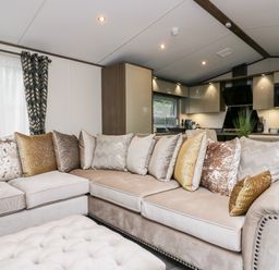 A living area with a beige sectional sofa and multiple decorative pillows next to a kitchen with cabinets and appliances at 43 Pony Meadow in Troutbeck Bridge