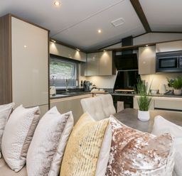 A kitchen and dining area with a sofa featuring multiple pillows and cabinets with appliances at 43 Pony Meadow in Troutbeck Bridge