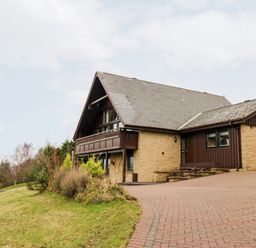 Exterior view of a house with a stone and wood facade and a sloped roof with a driveway and grass lawn at Slaley Park Villa in Hexham