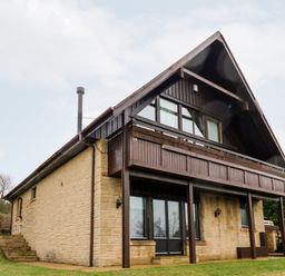 A two story house with stone lower walls and wooden upper walls with a balcony in a grassy area at Slaley Park Villa in Hexham
