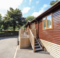 A wooden lodge with a small staircase and trees nearby at JacMar Lodge 14 Applethwaite Limefitt Park near Windermere