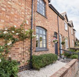 Brick exterior of a row of houses with gray window frames and doors with plants and flowers outside at Ross Cottage in Broadway