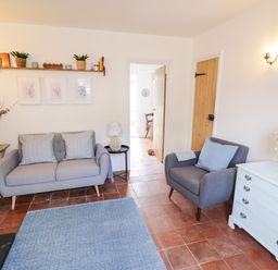 A living room with a sofa armchair shelf white dresser and flowers at Ross Cottage in Broadway