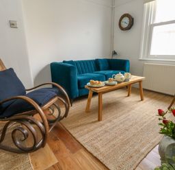A living room with a blue sofa a wooden rocking chair a wooden coffee table with tea and pastries a clock on the wall and a plant at 26 High West in Weymouth