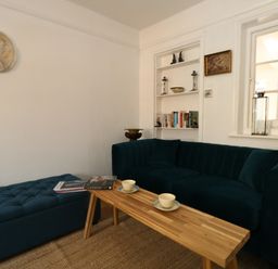 A living room with a blue sofa and ottoman a wooden coffee table with cups and books and a bookshelf at 26 High West in Weymouth