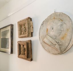 A white wall with three wooden framed decorations and a round relief sculpture of a man in profile at 26 High West in Weymouth